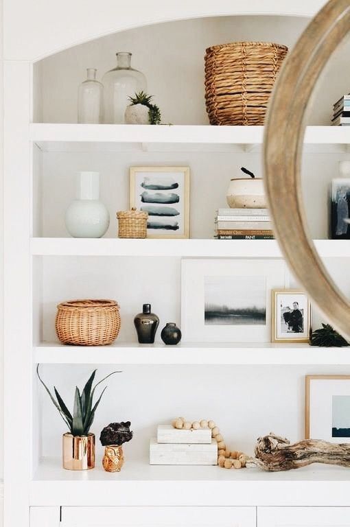 a white shelf with pictures, books and other items on it's shelves next to a mirror