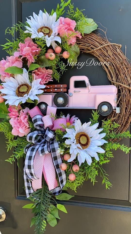 a wreath with flowers and a pink truck is hanging on the front door for someone to welcome