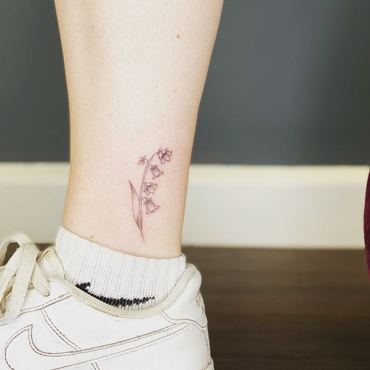 a small flower tattoo on the ankle by a woman's foot with white sneakers