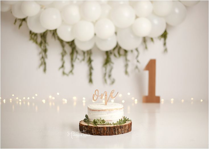 a white cake sitting on top of a table next to a number one balloon wall