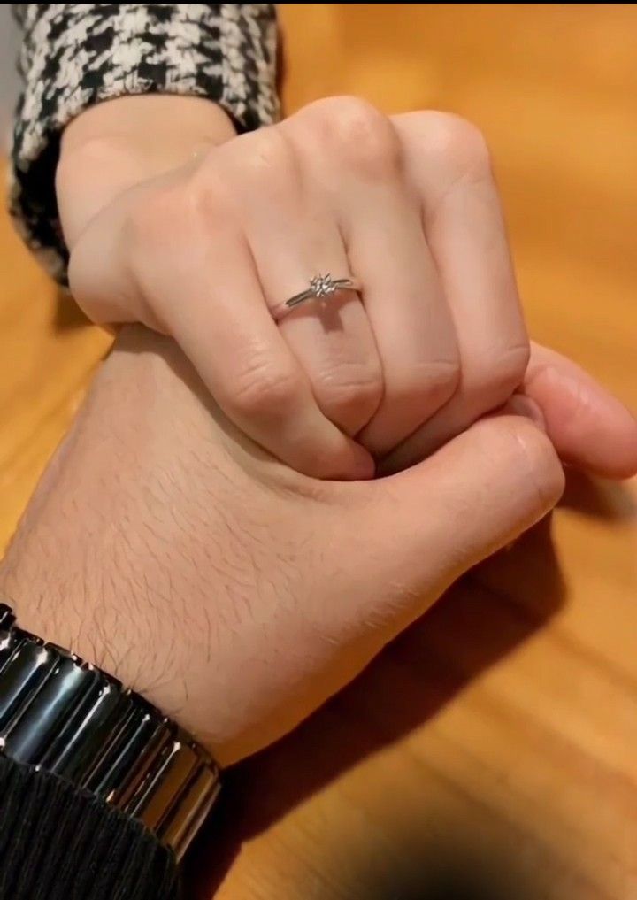 a person wearing a ring on their wrist holding the other hand with both hands, while sitting at a table