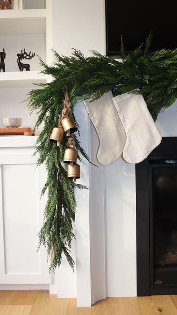 stockings hanging from a christmas tree in front of a fireplace with bells and evergreen branches