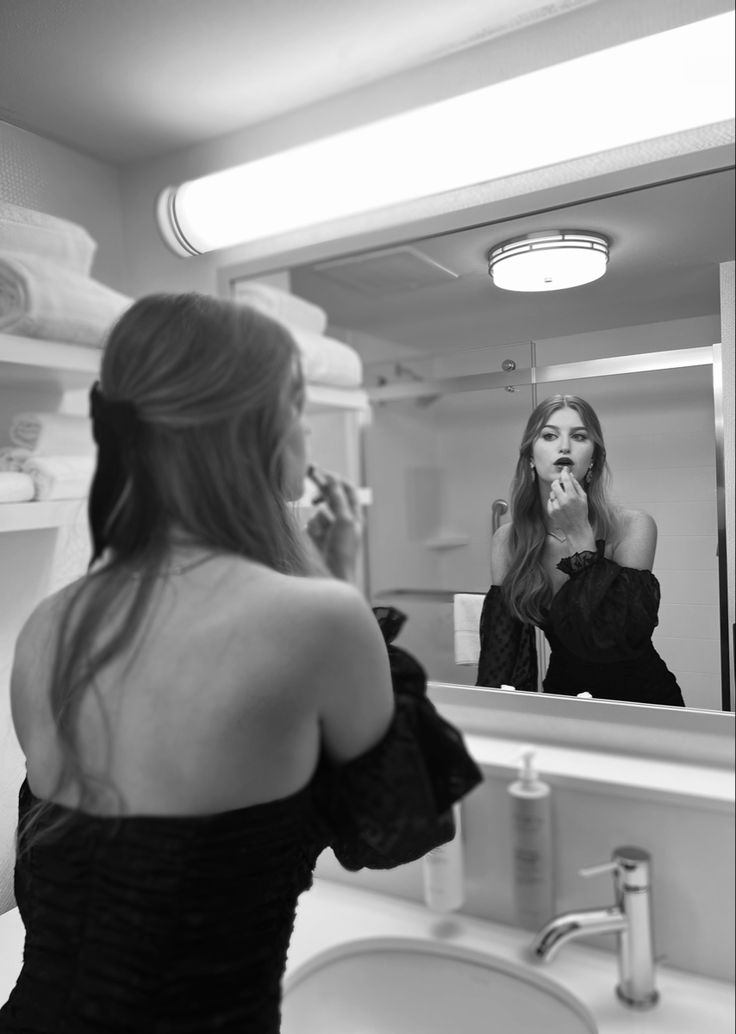 a woman brushing her teeth in front of a bathroom mirror while looking at herself in the mirror