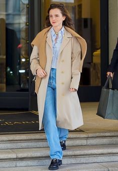 a woman is walking down the steps carrying shopping bags and wearing a trench coat with her hands in her pockets