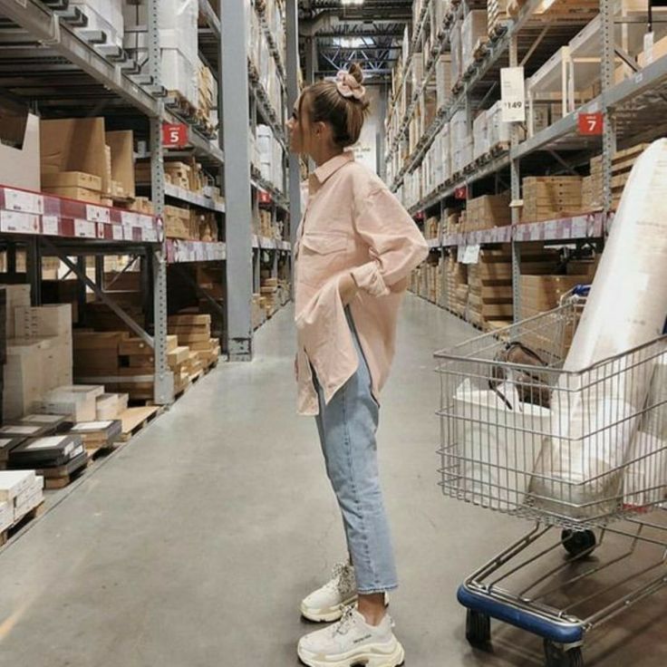 a woman standing in the middle of a warehouse with a shopping cart next to her