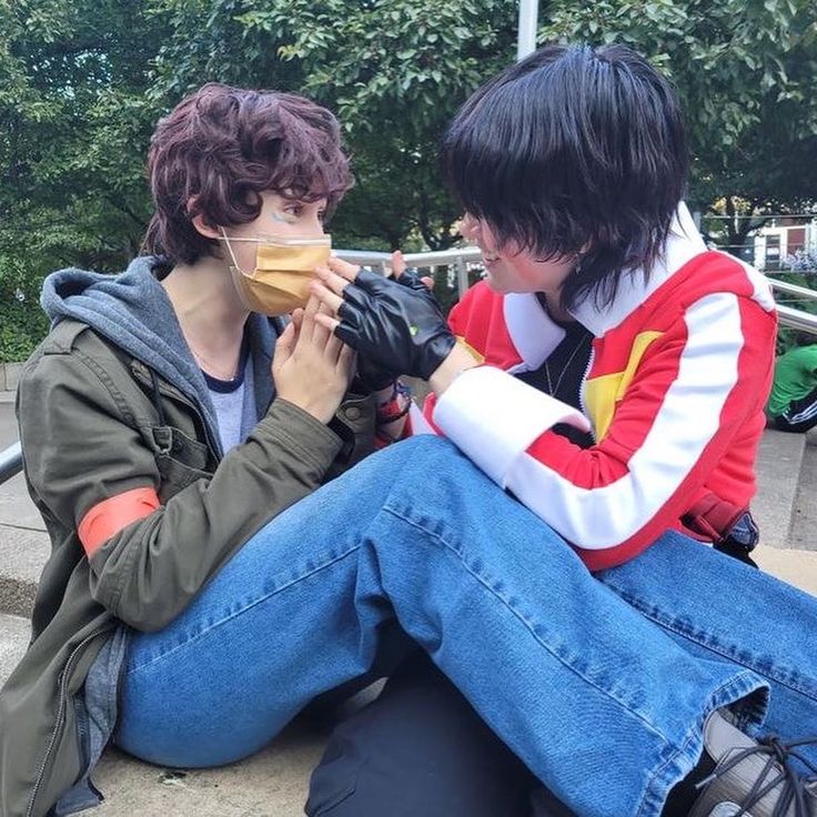 two people sitting on the ground with one holding something in his mouth and the other wearing a face mask