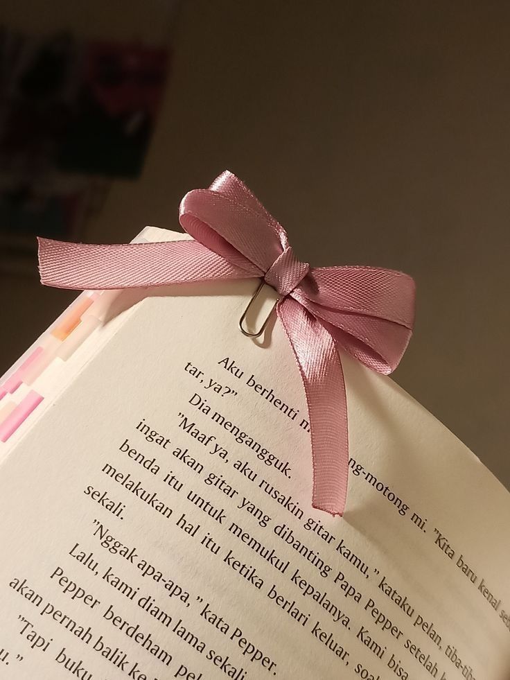 an open book with a pink ribbon tied around the page and some writing on it