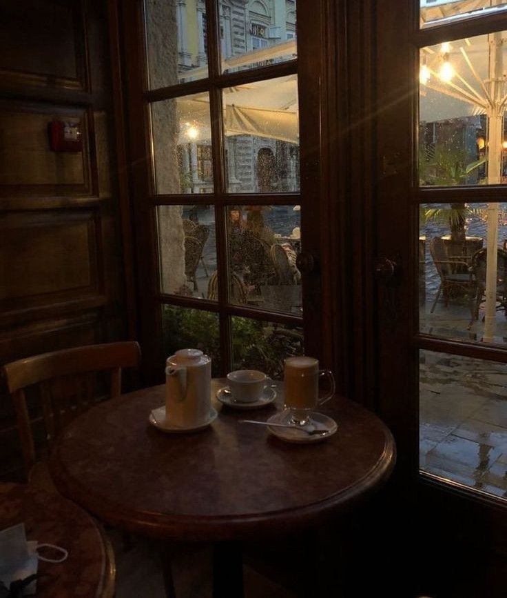 two cups of coffee sit on a table in front of an open window