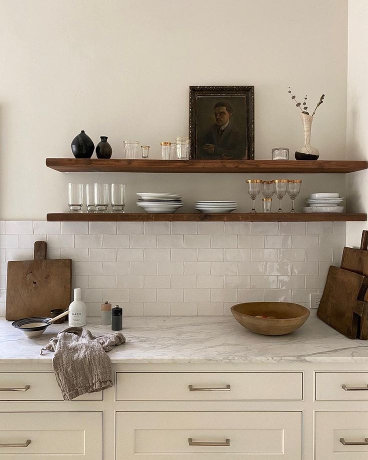 a kitchen with white cabinets and shelves filled with dishes on top of each other in front of a painting