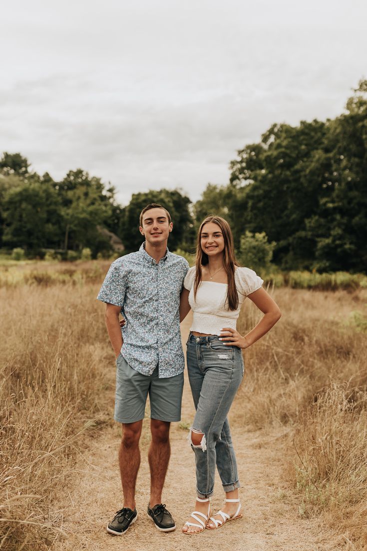 a young man and woman standing on a dirt path in the middle of a field