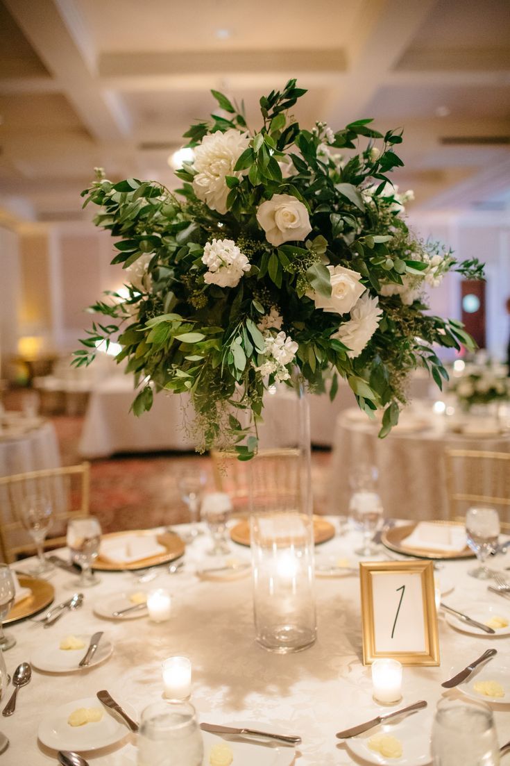 the centerpieces on this table are all white flowers and greenery, along with candles