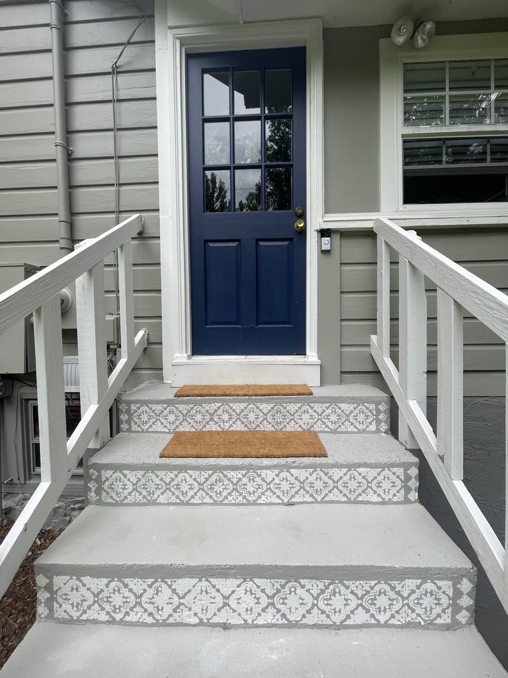 a blue door and some steps in front of a gray house with white railings