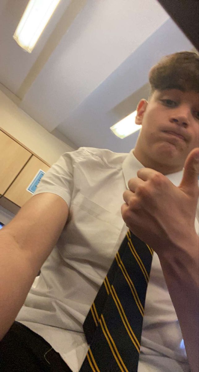 a young man wearing a white shirt and yellow striped tie making a thumbs up gesture