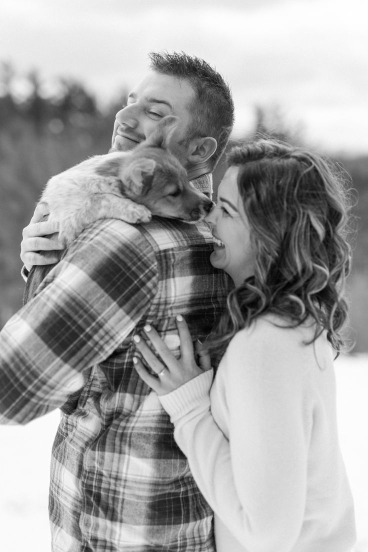 a man holding a dog in his arms while standing next to a woman with her eyes closed