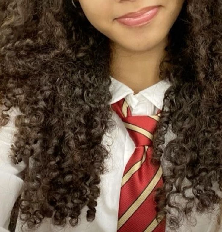 a woman with long curly hair wearing a tie and dress shirt is looking at the camera