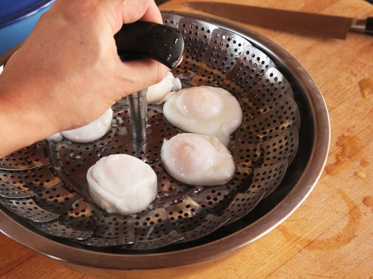 a person is frying eggs in a strainer on a wooden table with utensils