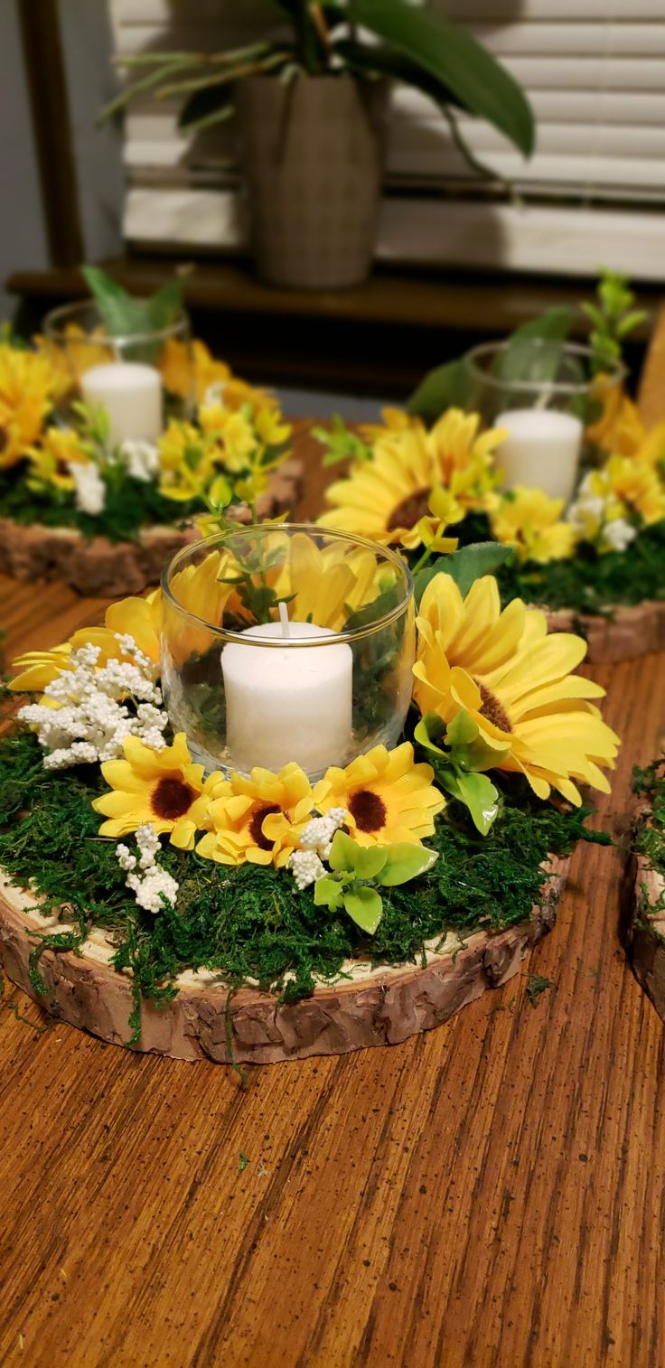 sunflowers and greenery are arranged around a candle holder on a wooden table