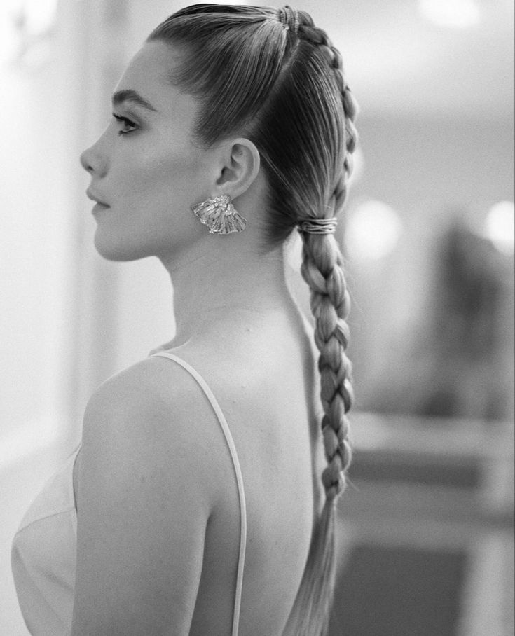 a black and white photo of a woman with long hair in a ponytail wearing earrings