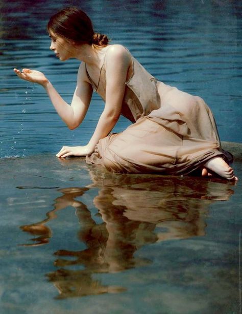 a woman kneeling in the water with her hand out to touch something on her chest