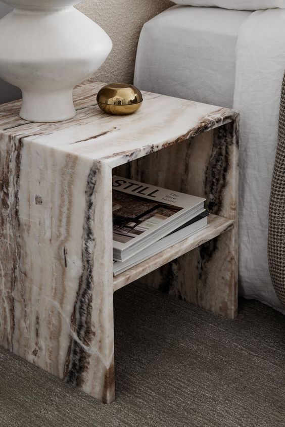 a marbled end table with magazines on it next to a white vase and bed