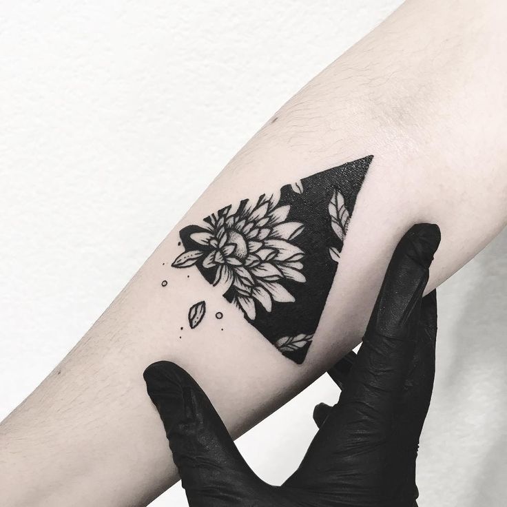 a woman's arm with a black and white flower tattoo on the left forearm