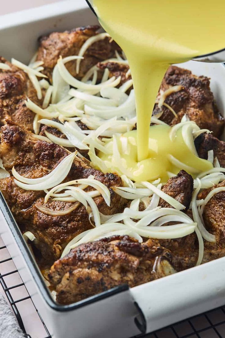 someone is pouring sauce on some food in a pan with onions and meatballs inside