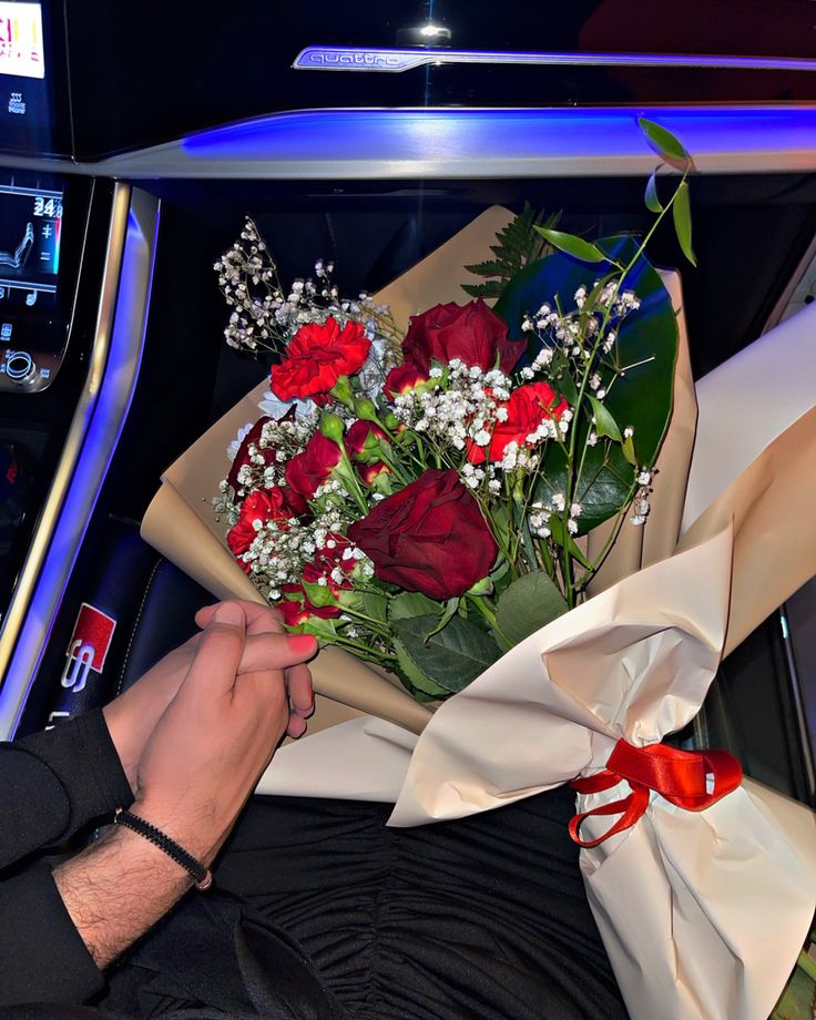 a bouquet of red roses is being held in the back of a car by someone's hand