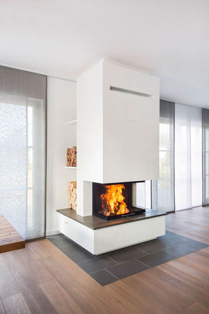 a modern fireplace in the middle of a living room with wood floors and white walls