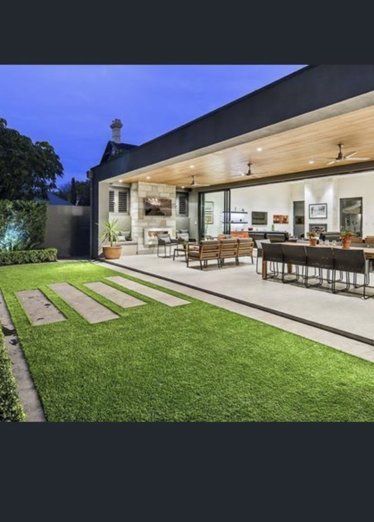 an outdoor living room and dining area are lit up at night, with grass in the foreground