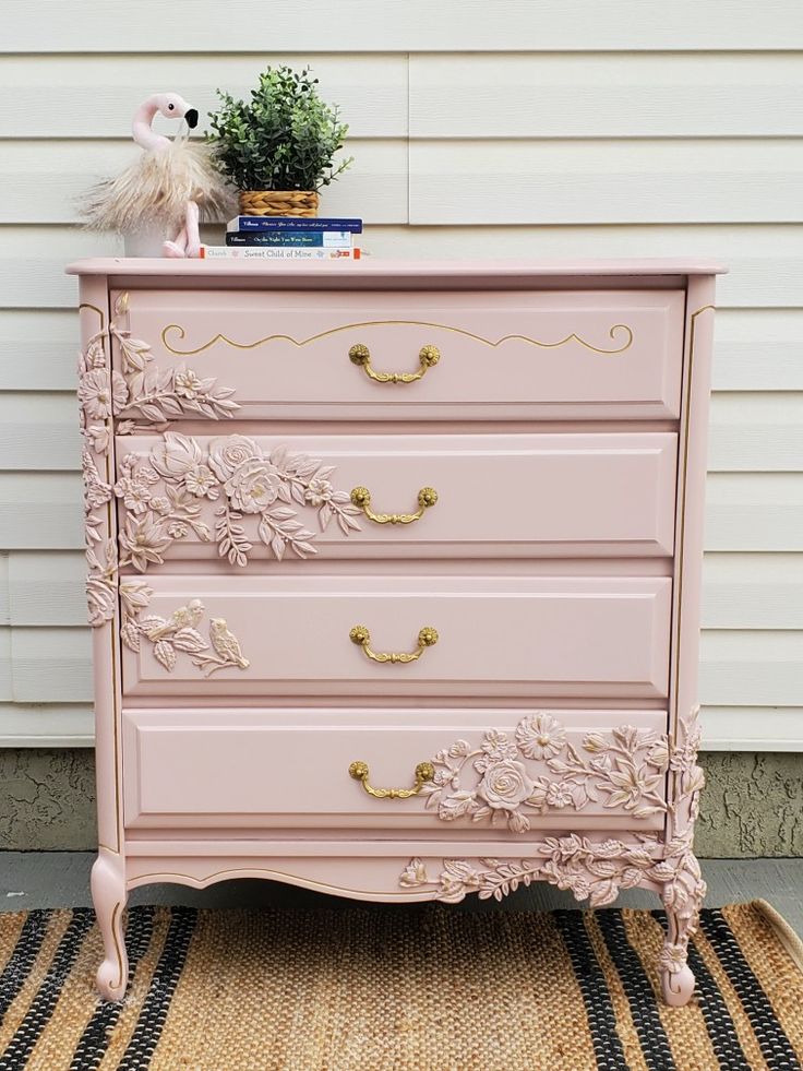 a pink dresser sitting on top of a rug next to a white house with a potted plant