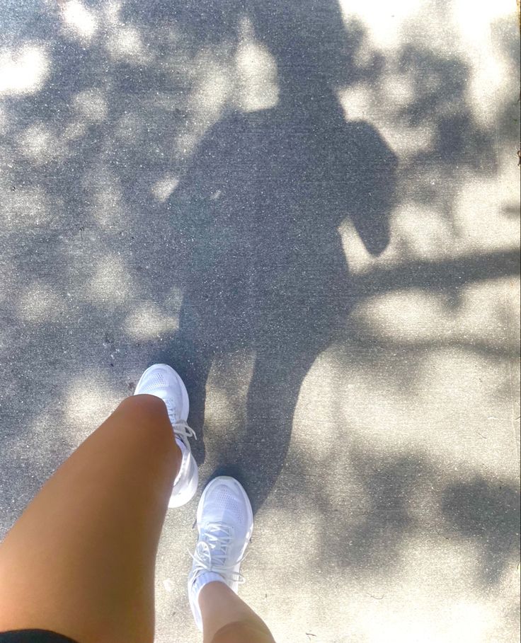 the shadow of a person standing next to a skateboarder on cement ground with trees in the background