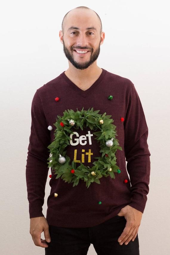 a man wearing a christmas wreath sweater with the words get lit written on it in front of his face