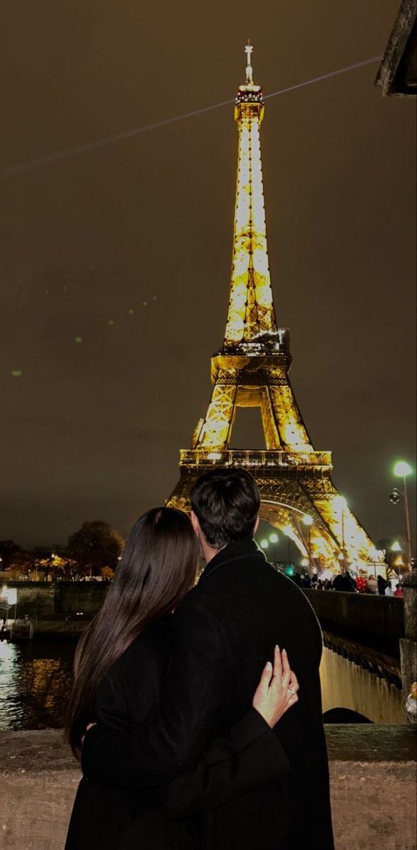 a man and woman are hugging in front of the eiffel tower at night