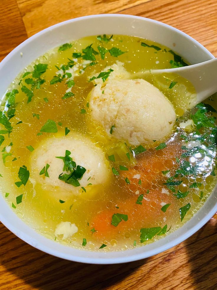 a bowl filled with soup and dumplings on top of a wooden table