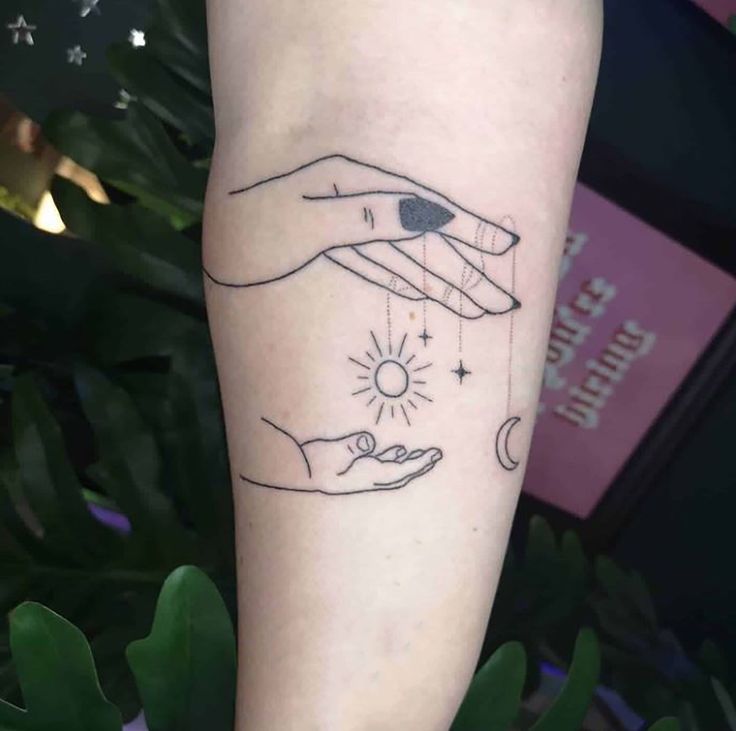 two hands touching each other with the sun and moon above them on a woman's arm