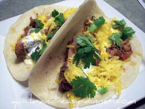 two tacos with meat, cheese and cilantro on a white square plate