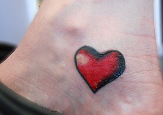 a small heart tattoo on the foot of a woman's left ankle, which is red and black