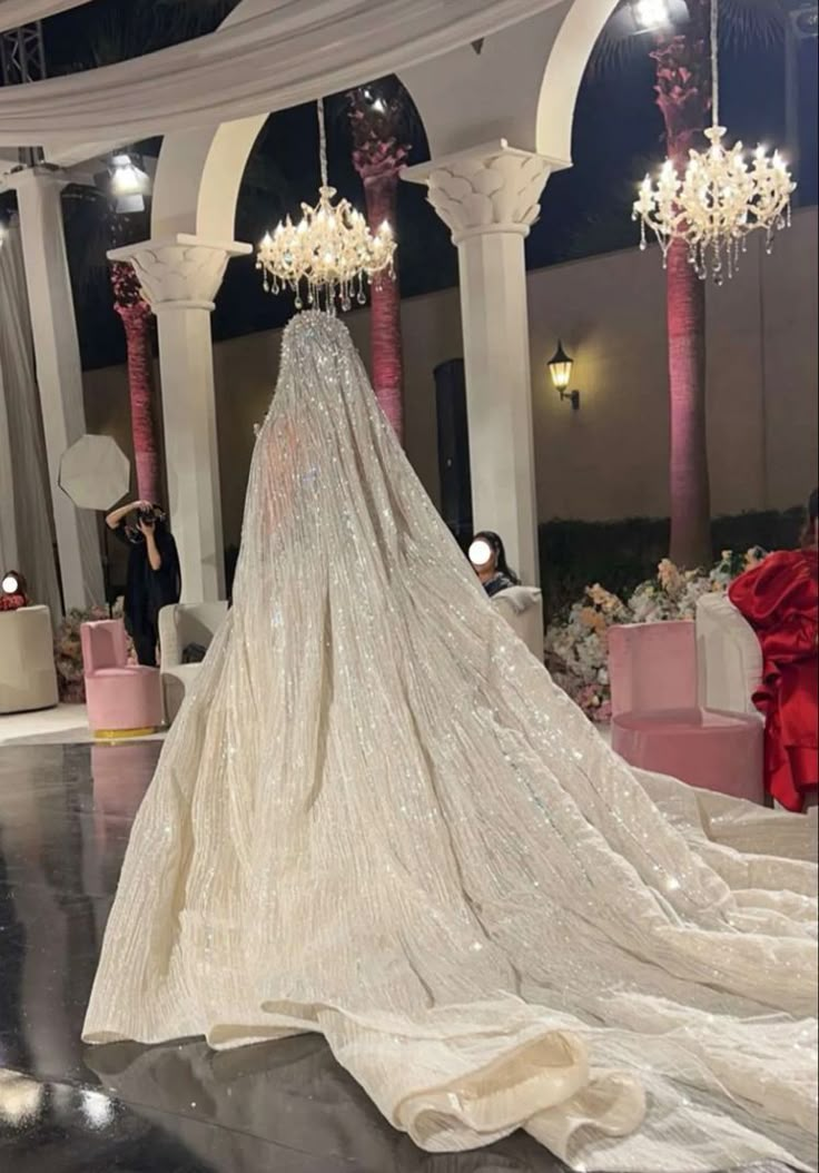 the back of a wedding dress on display in a room with columns and chandeliers