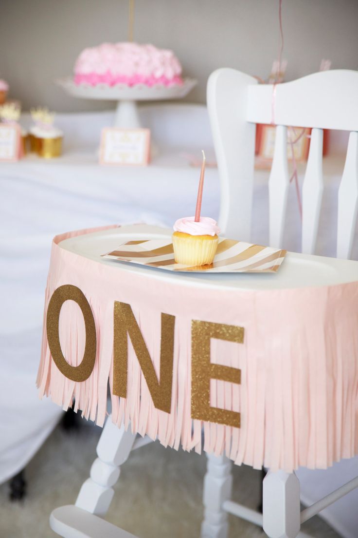 a pink and gold first birthday party with cupcakes on the table, one candle in the middle