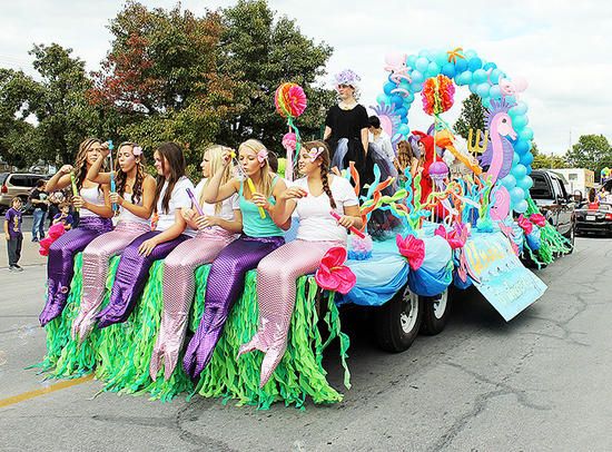 a group of women riding on the back of a float in a parade down a street