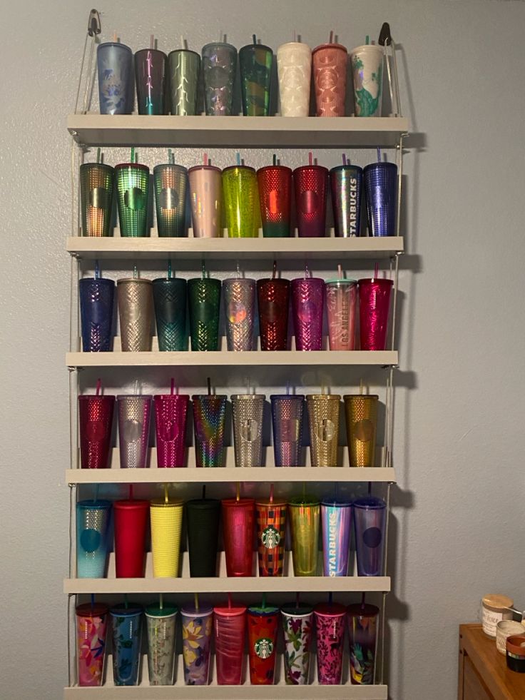 a shelf filled with lots of different colored cups on top of each other in front of a white wall