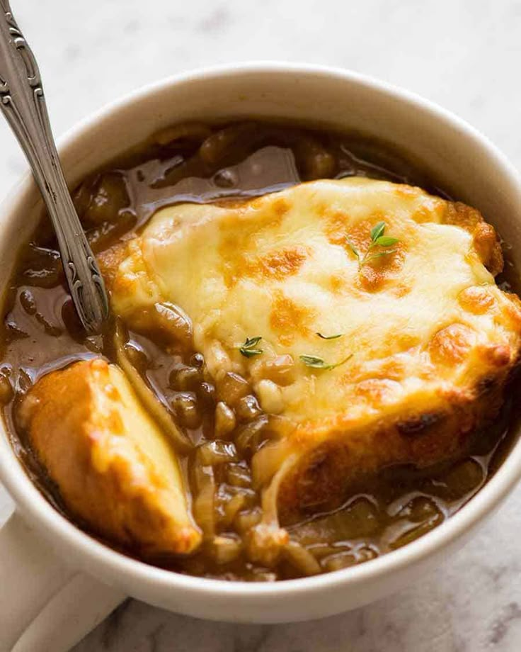 a bowl filled with meat and beans on top of a white tablecloth next to a fork