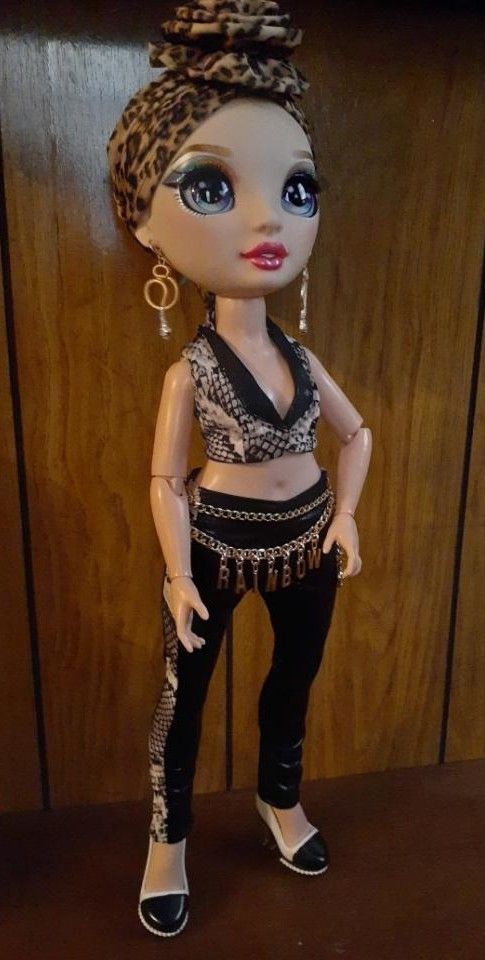 a doll with big blue eyes wearing black pants and a leopard print headband