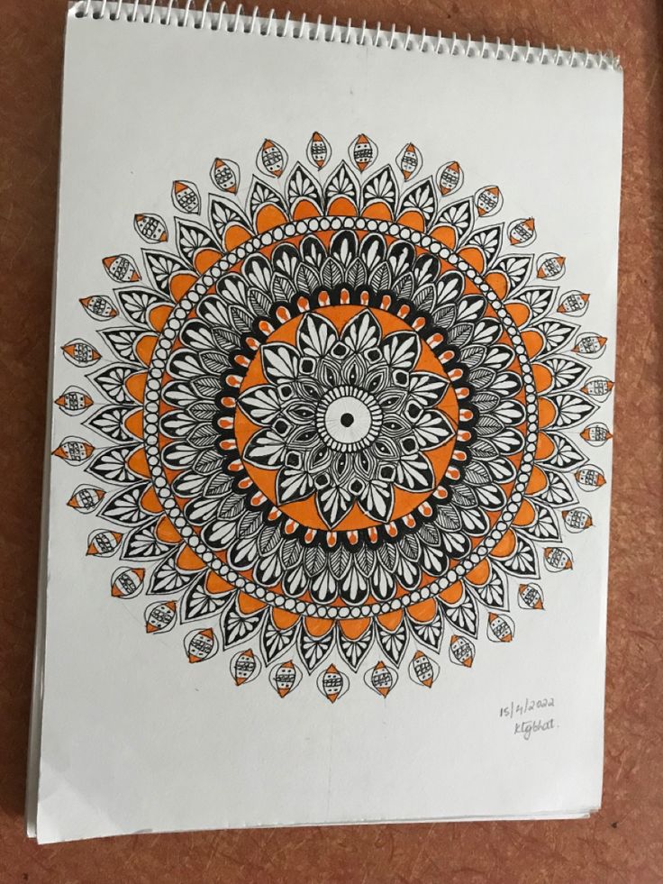 an orange and black drawing on white paper next to a brown table top with a pen