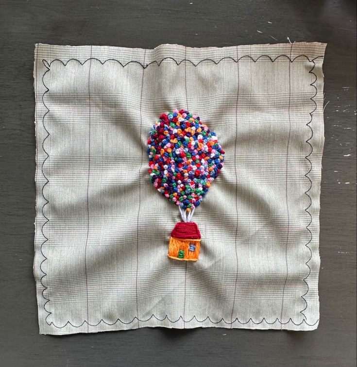 a piece of cloth with beads on it and a small house hanging from the side