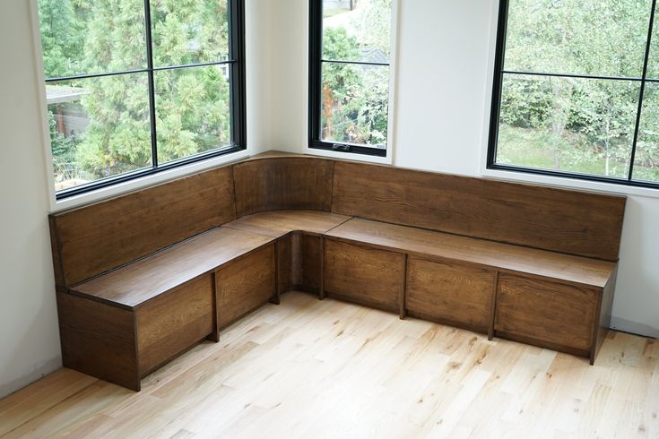 a corner bench in the middle of a room with three windows and wood flooring