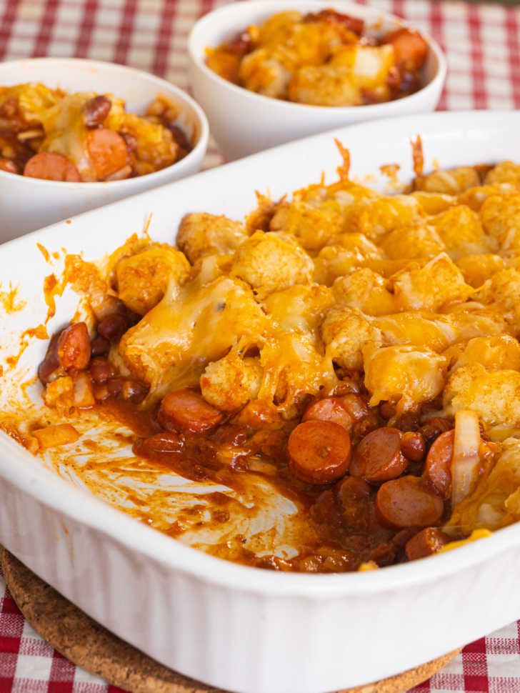 a casserole dish with sausage, beans and cheese in it on a checkered tablecloth