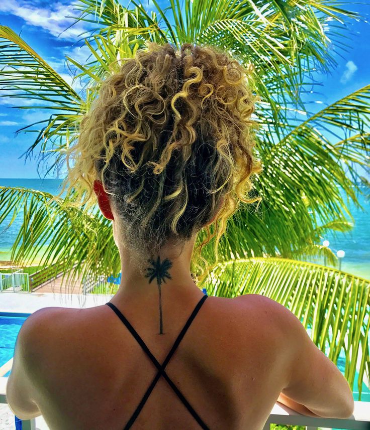 a woman with her back turned to the camera, looking out at the ocean and palm trees