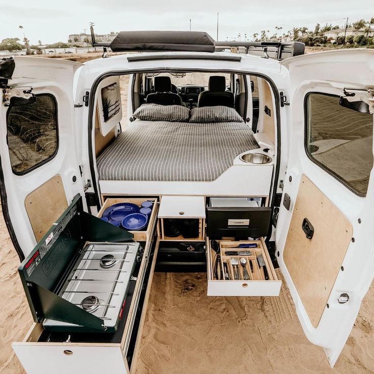 the back end of a van with its doors open and drawers opened on the beach