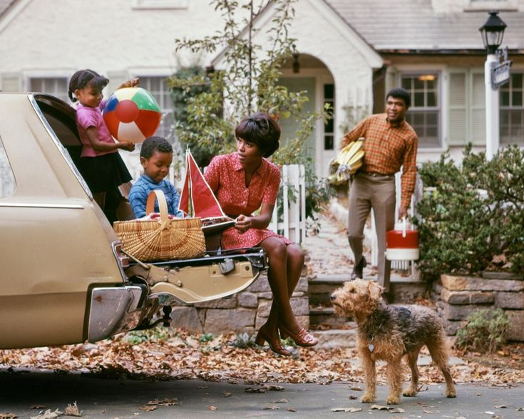 a woman sitting in the back of a car with two children and a dog next to her